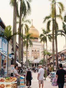 Street view of the Sultan Mosque golden dome in Kampong Glam, Singapore, framed by palm trees